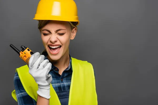 Angry builder in hardhat screaming while holding walkie talkie isolated on grey — Stock Photo