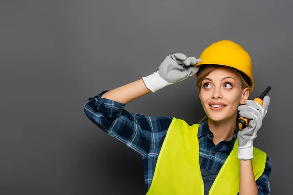 Blonde builder in safety vest holding walkie talkie on grey background — Stock Photo