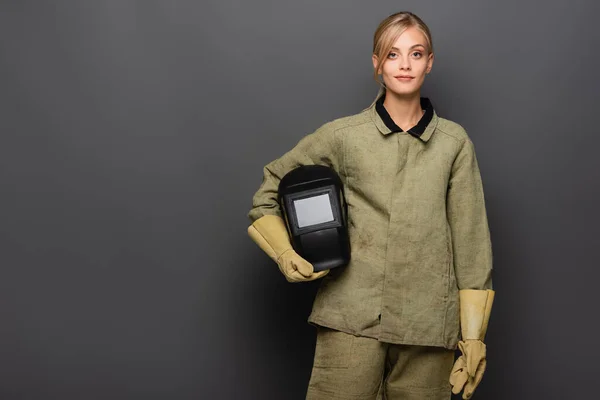 Soldador rubio con guantes sosteniendo el casco sobre fondo gris - foto de stock