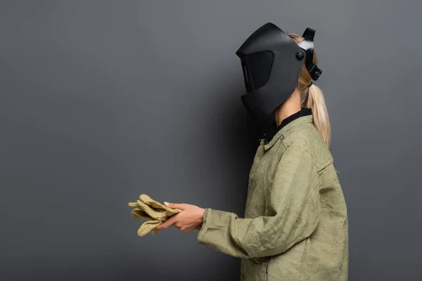 Blonde welder in mask and uniform holding gloves on grey background — Stock Photo