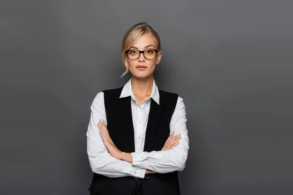 Pretty businesswoman standing with crossed arms and looking at camera isolated on grey — Stock Photo