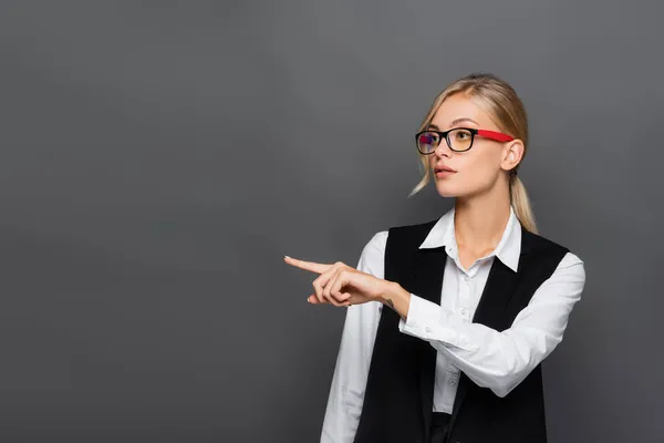 Femme d'affaires blonde aux lunettes pointant du doigt isolé sur gris — Photo de stock