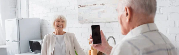 Hombre mayor sosteniendo teléfono inteligente con pantalla en blanco cerca de un amigo sonriente en el hogar de ancianos, pancarta - foto de stock