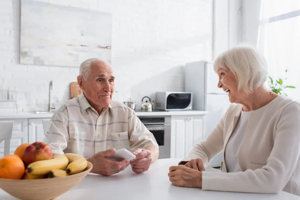 Smiling senior woman looking at friend with smartphone in nursing home — Stock Photo