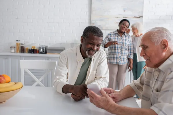 Älterer Mann benutzt Smartphone neben lächelndem afrikanisch-amerikanischem Freund in Pflegeheim — Stockfoto