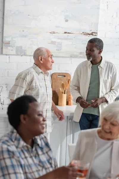 Les hommes interraciaux âgés parlent près des femmes floues dans la maison de retraite — Photo de stock