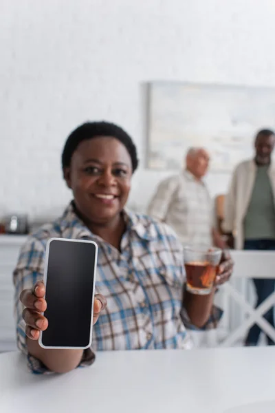 Smartphone en main d'une femme afro-américaine floue avec du thé dans une maison de retraite — Photo de stock