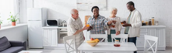 Personas mayores interraciales positivas con té y teléfono inteligente en el hogar de ancianos, pancarta - foto de stock