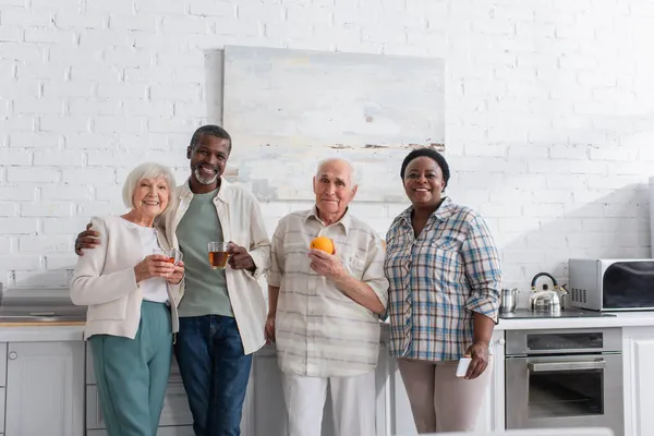 Fröhliche multiethnische Senioren mit Tee und Smartphone in der Küche des Pflegeheims — Stockfoto