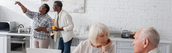 Senior afrikanisch-amerikanische Frau mit Smartphone zeigt mit dem Finger nahe Freund mit Obst in Pflegeheim, Banner — Stockfoto