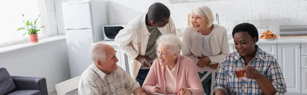 Personas multiétnicas positivas con teléfono inteligente y té hablando en el hogar de ancianos, pancarta - foto de stock