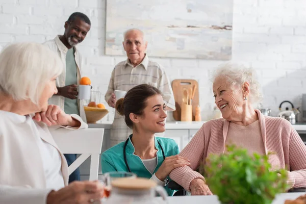 Lächelnde Krankenschwester schaut Seniorin in der Nähe von Patienten im Pflegeheim an — Stockfoto