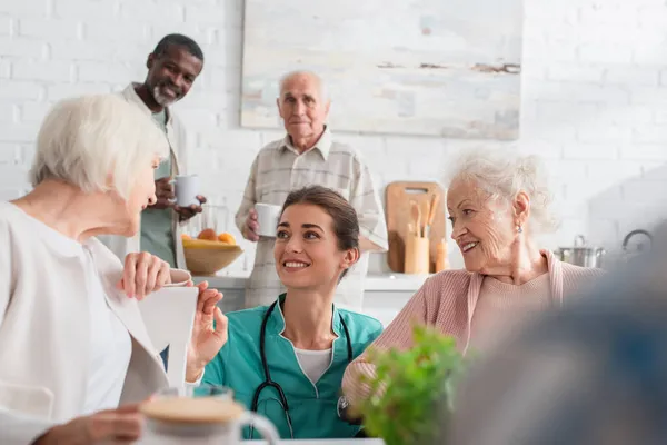 Молода медсестра проводить час зі усміхненими міжрасовими пацієнтами в будинку престарілих — стокове фото