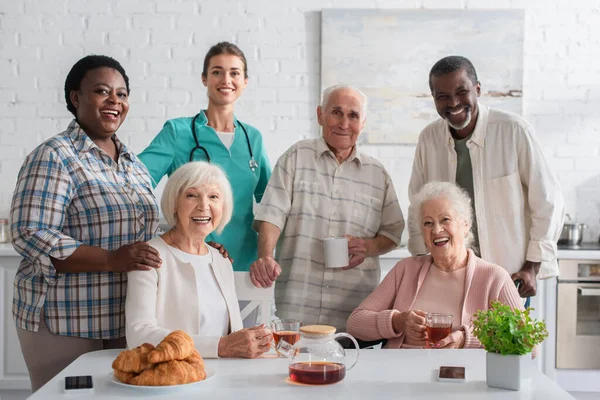 Lächelnde Krankenschwester steht neben Patienten und Tee im Pflegeheim — Stockfoto