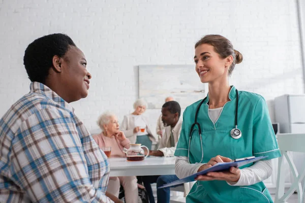 Young nurse holding clipboard near senior african american patient in nursing home — Stock Photo