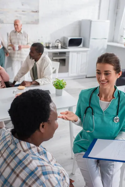 Krankenschwester mit Klemmbrett im Gespräch mit afrikanisch-amerikanischer Patientin im Pflegeheim — Stockfoto