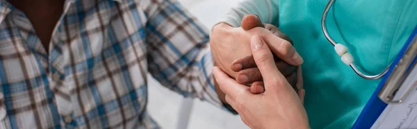 Ausgeschnittene Ansicht einer Krankenschwester, die die Hand eines afrikanisch-amerikanischen Patienten im Pflegeheim hält, Banner — Stockfoto