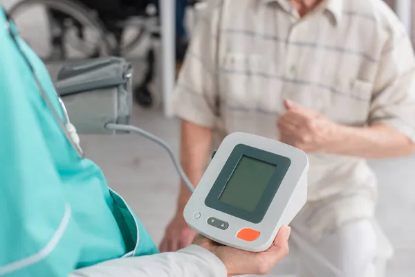 Ausgeschnittene Ansicht einer Krankenschwester, die Tonometer in der Nähe einer Seniorin im Pflegeheim hält — Stockfoto