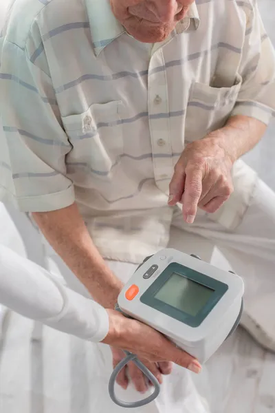 Ausgeschnittene Ansicht eines älteren Mannes, der auf Tonometer in der Nähe von Krankenschwester in Pflegeheim zeigt — Stockfoto