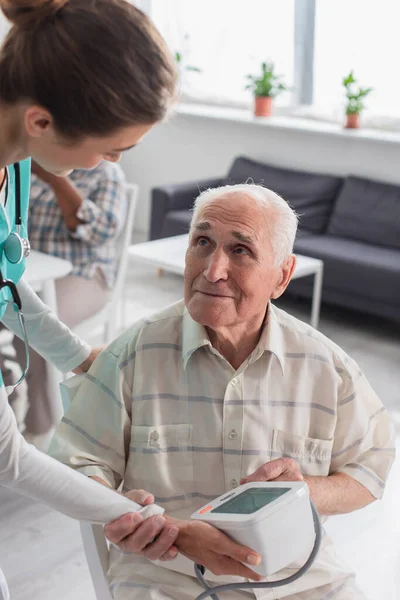 Enfermera sosteniendo tonómetro cerca de anciano en casa de ancianos — Stock Photo