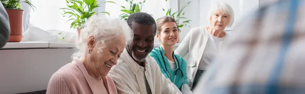 Pensionati multietnici sorridenti e infermiera in casa di cura, striscione — Foto stock