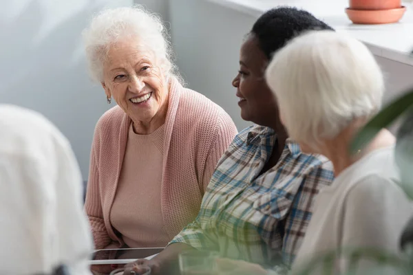 Мультиэтнические пожилые женщины с цифровыми планшетами разговаривают в доме престарелых — стоковое фото