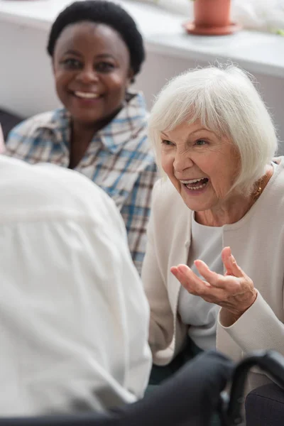 Позитивная женщина разговаривает с размытой подругой в доме престарелых — стоковое фото