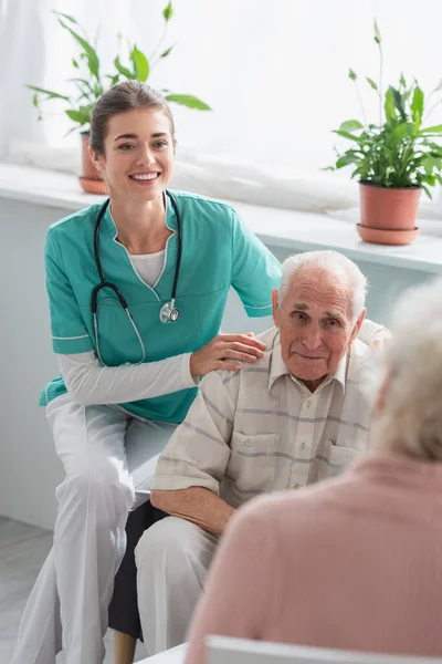 Enfermera feliz abrazando a paciente mayor en hogar de ancianos - foto de stock
