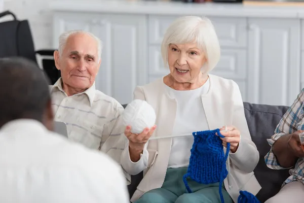 Elderly woman holding yarn near interracial friends in nursing home — Stock Photo