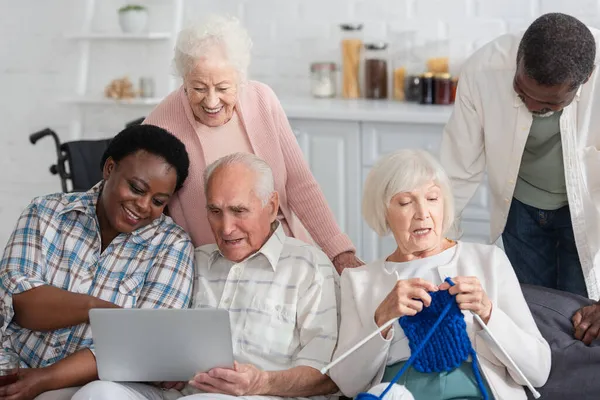 Senior interracial pensioners spending time with yarn and laptop in nursing home — Stock Photo