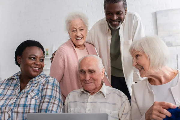 Happy multiethnic pensioners with yarn and laptop spending time in nursing home — Stock Photo