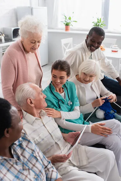 Nurse sitting near interracial patients with digital tablet and yarn in nursing home — Stock Photo