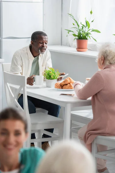 Homme afro-américain avec thé et smartphone parlant à un ami dans une maison de retraite — Photo de stock