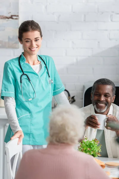 Lächelnde Krankenschwester steht neben interrassischen Patienten im Pflegeheim — Stockfoto