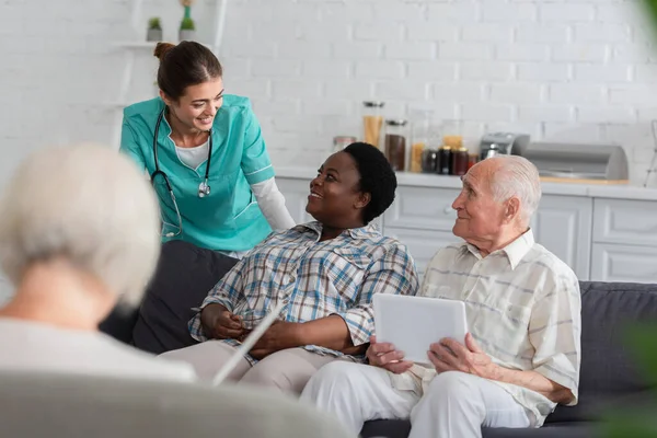 Позитивна медсестра розмовляє з афріканською жінкою з чаєм біля старших пацієнтів у будинку престарілих. — стокове фото