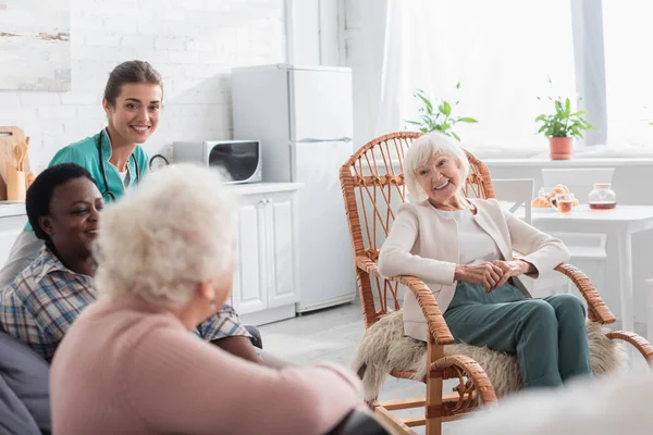 Веселі старші міжрасові жінки проводять час біля молодої медсестри в будинку престарілих — стокове фото