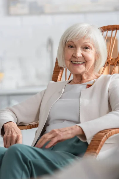 Весела старша жінка дивиться на камеру в кріслі для качання в будинку престарілих — стокове фото
