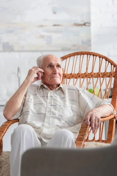 Uomo dai capelli grigi che distoglie lo sguardo sulla sedia a dondolo nella casa di cura — Foto stock