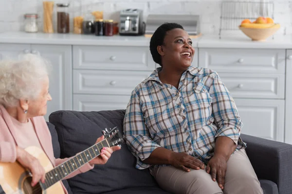 Mujer afroamericana cantando cerca de un amigo mayor tocando la guitarra acústica en un hogar de ancianos - foto de stock