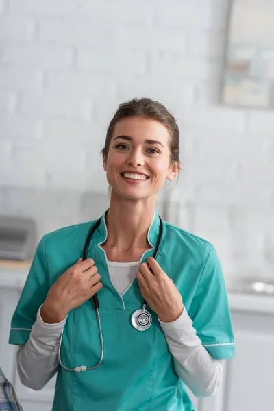 Enfermeira sorridente de uniforme segurando estetoscópio em casa de repouso — Fotografia de Stock