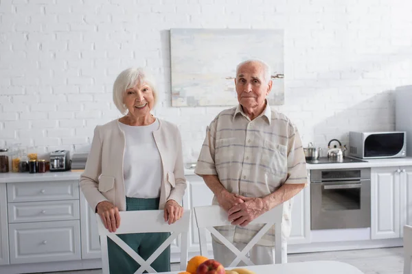 Усміхнені літні люди дивляться на камеру на кухні будинку престарілих — стокове фото