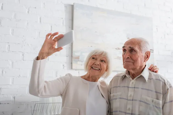 Ältere Frau macht Selfie mit Smartphone in der Nähe von Seniorenfreund im Pflegeheim — Stockfoto