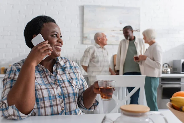 Sorridente donna afroamericana in possesso di tazza e parlando su smartphone in casa di cura — Foto stock