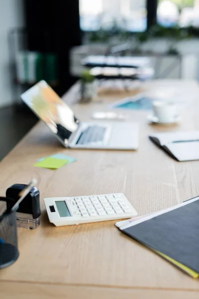 Taschenrechner neben Papiermappe und verschwommenem Laptop auf Tisch im Büro — Stockfoto