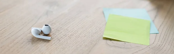 Earphones near sticky notes on table in office, banner — Stock Photo