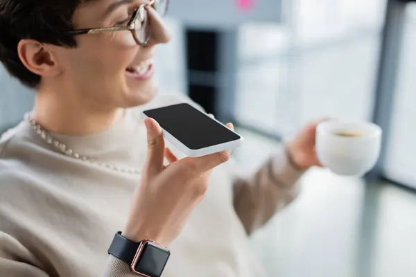 Смартфон с чистым экраном в руке улыбающегося бизнесмена с чашкой голосового сообщения в офисе — стоковое фото