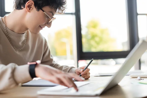 Vista laterale di un uomo d'affari sorridente che scrive su un notebook e utilizza un computer portatile in ufficio — Foto stock