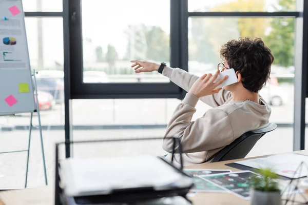 Uomo d'affari che parla su smartphone vicino a flip chart offuscata in ufficio — Foto stock