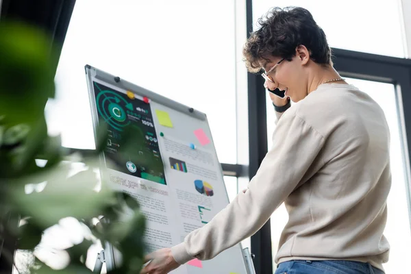 Vista laterale dell'uomo d'affari che parla sul telefono cellulare vicino al flip chart in ufficio — Foto stock