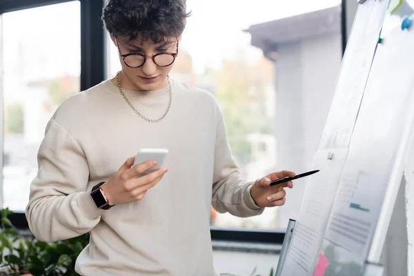 Giovane uomo d'affari che utilizza il cellulare vicino a flip chart in ufficio — Foto stock